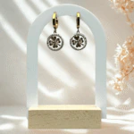 Boucles d'oreilles pendantes médaillon trèfle doré et strass sur présentoir arche blanc