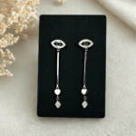 Boucles d'oreilles pendantes œil protecteur argentées présentées sur une carte noire