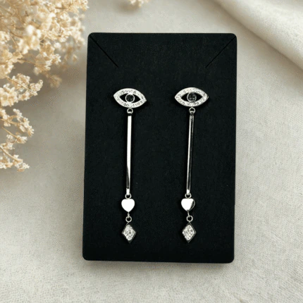 Boucles d'oreilles pendantes œil protecteur argentées présentées sur une carte noire