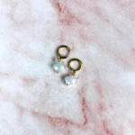 Créoles fines dorées femme à pendentif trèfle en cristal irisé facetté, posées sur marbre rose