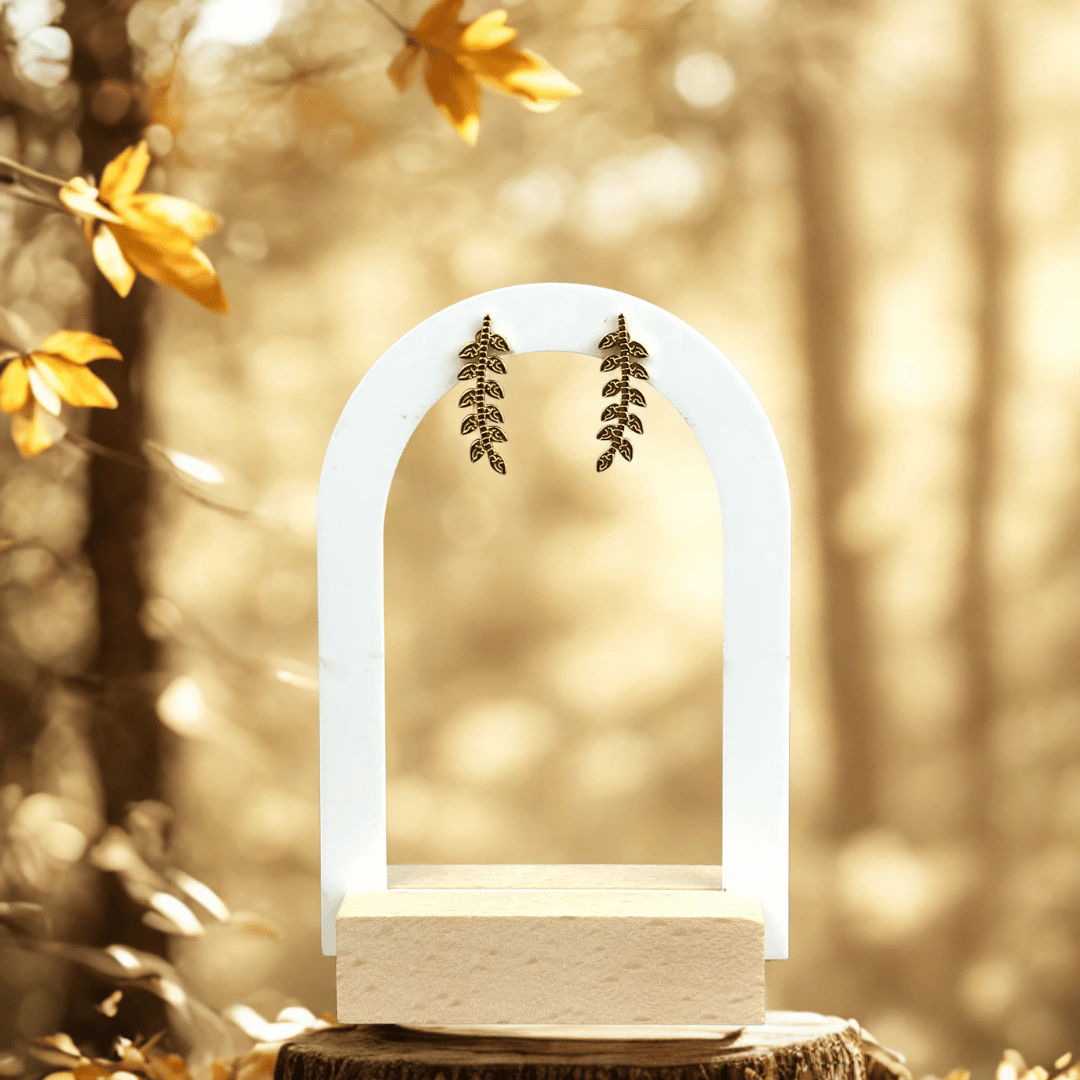 Clous d'oreilles branche de feuilles dorées accrochés à un présentoir arche blanc, ambiance automnale