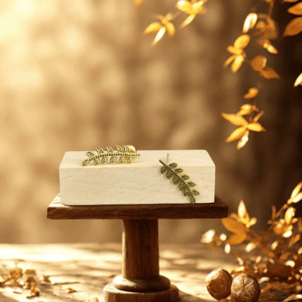 Clous d'oreilles dorés femme branche feuillue style grimpant, posés sur un socle dans un décor d'automne