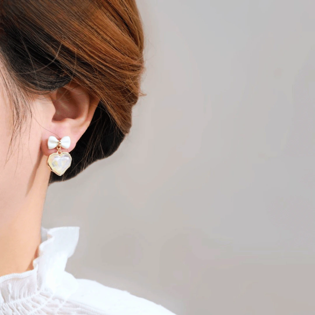 Femme portant une boucle d'oreille nœud blanc à pendentif cœur irisé doré, vue de profil