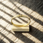 Bracelet jonc trèfle noir doré vu de dessus sur un socle en bois clair, jeu d'ombres