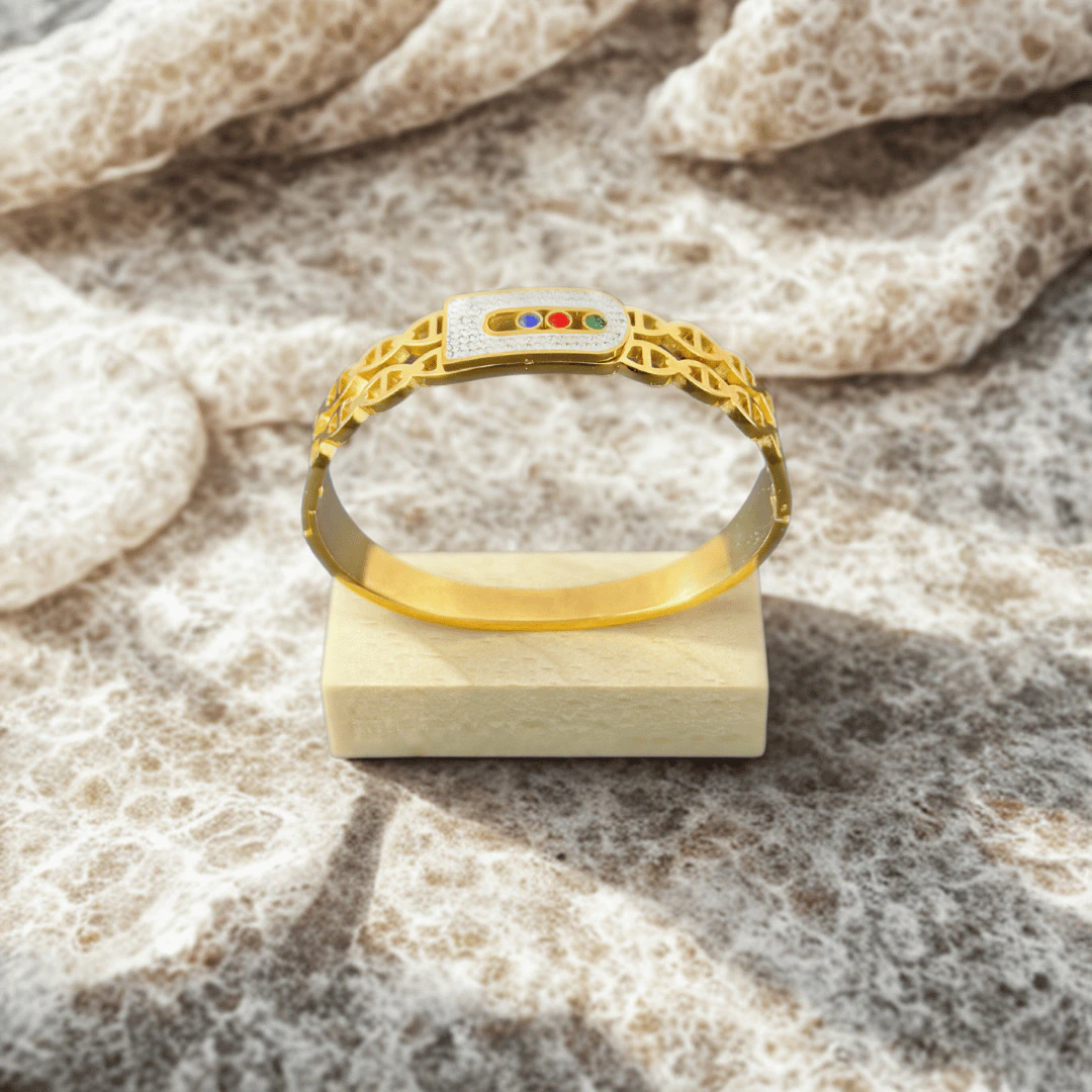 Bracelet jonc boucle scintillante doré posé sur un socle en bois, fond minéral texturé