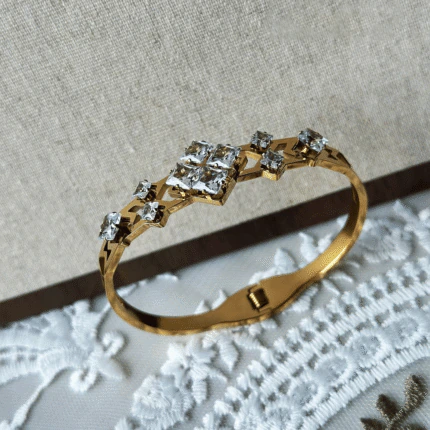 Bracelet jonc doré femme à mosaïque de cristaux carrés, design géométrique, posé sur dentelle blanche