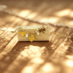 Breloques abeille, trèfle et libellule dorées du bracelet posé sur un bloc de bois au soleil