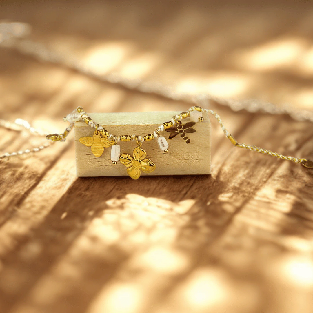 Breloques abeille, trèfle et libellule dorées du bracelet posé sur un bloc de bois au soleil