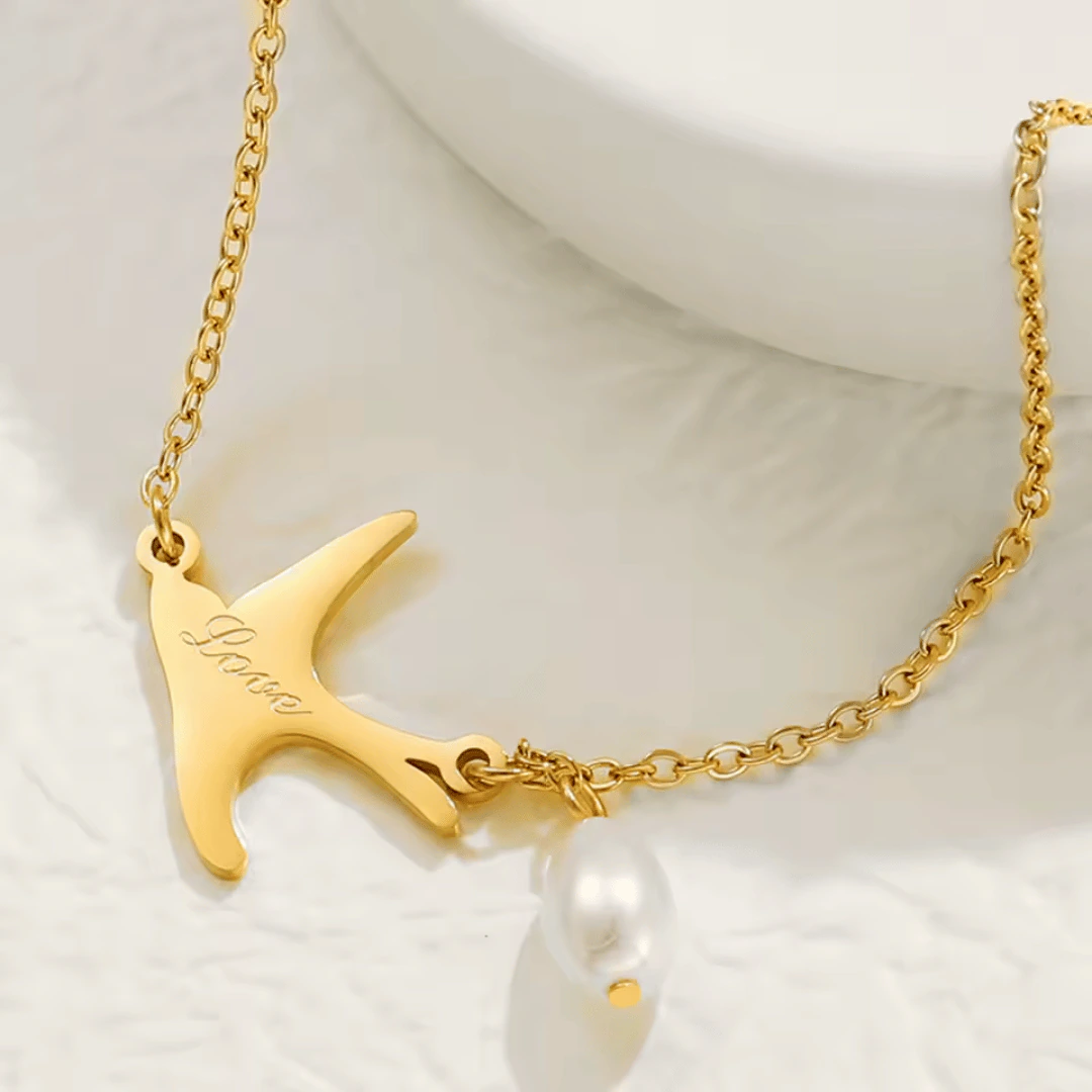 Gros plan sur l'hirondelle dorée gravée Love et la perle goutte blanche du bracelet chaîne fine