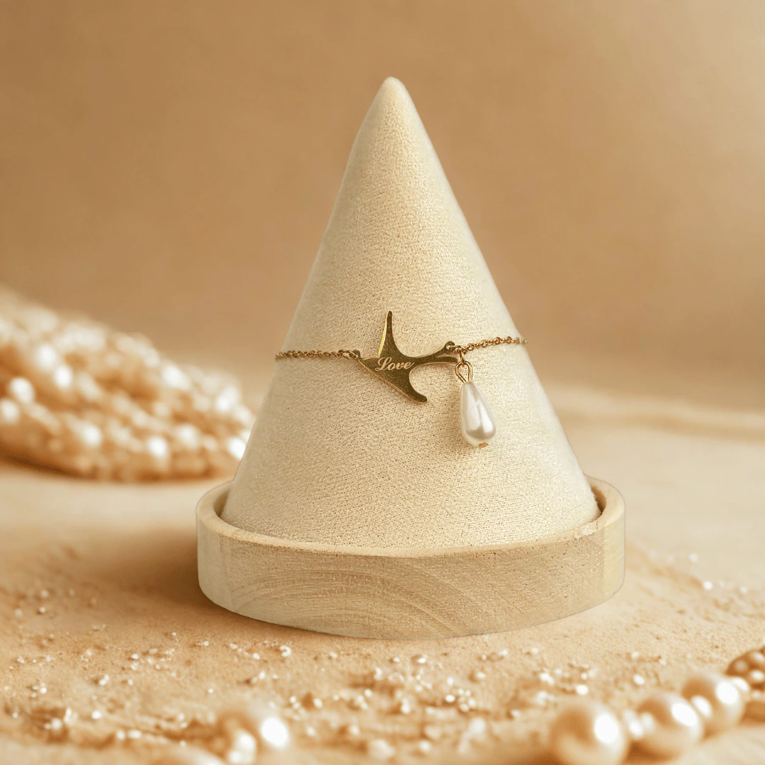 Bracelet hirondelle dorée et perle goutte présenté sur un cône en velours, décor de perles