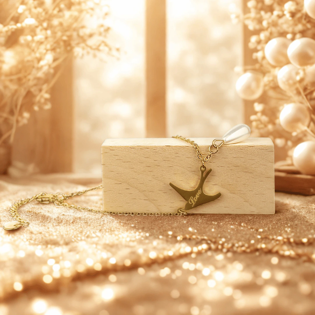 Bracelet chaîne fine hirondelle Love posé sur un bloc de bois, fond doré pailleté