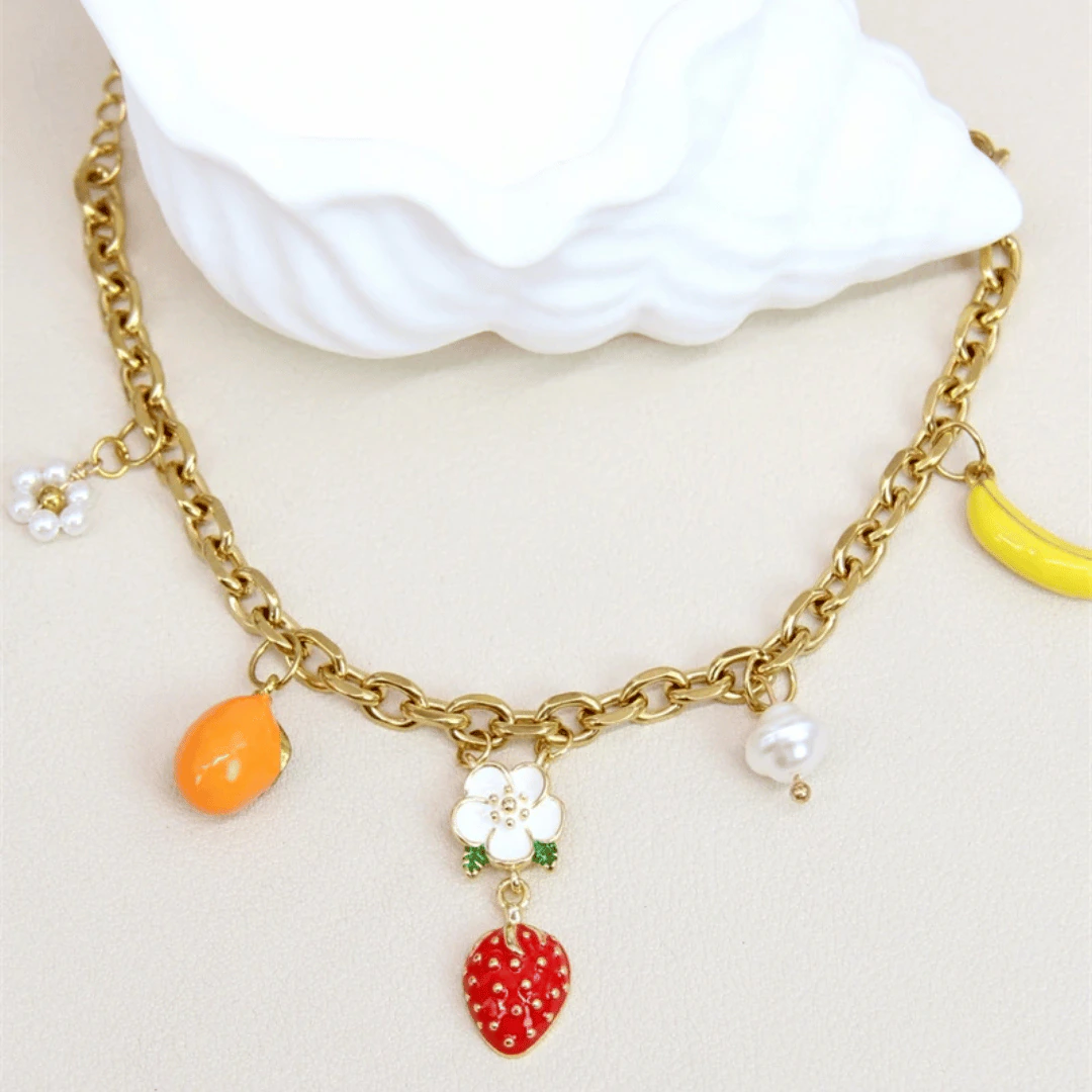 Vue rapprochée des charms fruits orange, fraise et banane et de la fleur blanche de la gourmette dorée