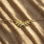 Bracelet laurier scintillant à feuilles dorées et rang de cristaux posé sur un tissu doré pailleté