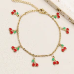Bracelet chaîne fine doré femme à charms cerises rouges et feuilles vertes, posé à plat
