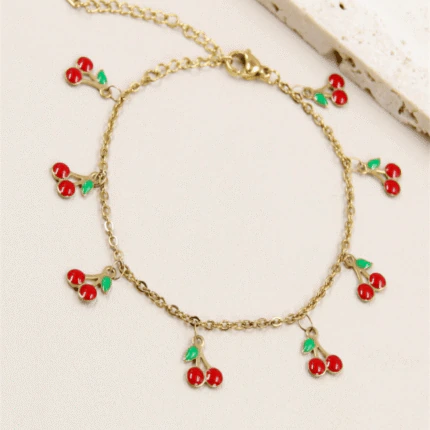 Bracelet chaîne fine doré femme à charms cerises rouges et feuilles vertes, posé à plat