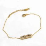 Bracelet chaîne fine dorée à barrette ovale scintillante posé à plat avec fermoir et chaînette de réglage