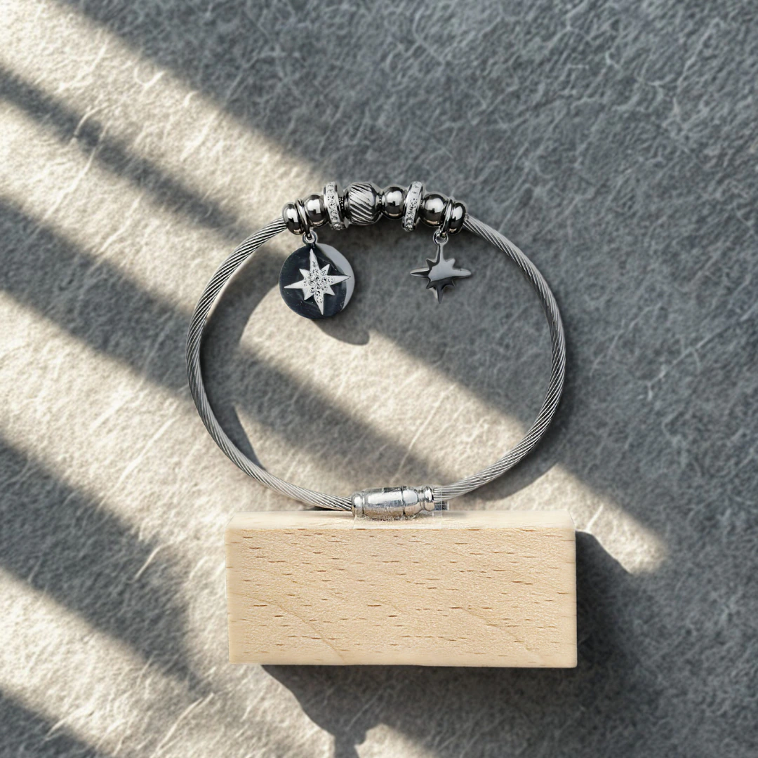 Bracelet jonc câble argenté à charms étoiles posé sur un socle en bois, jeu d'ombres et de lumière