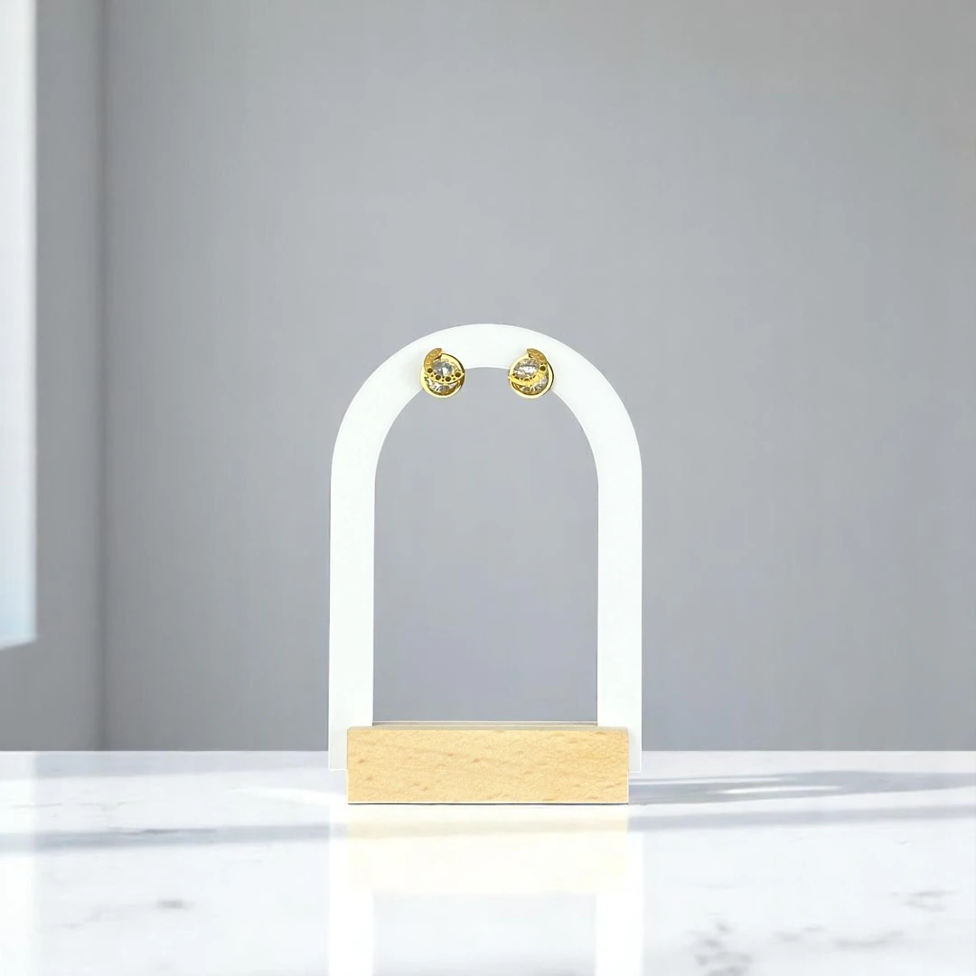 Puces d'oreilles dorées à cristal rond brillant présentées sur un présentoir arche blanc