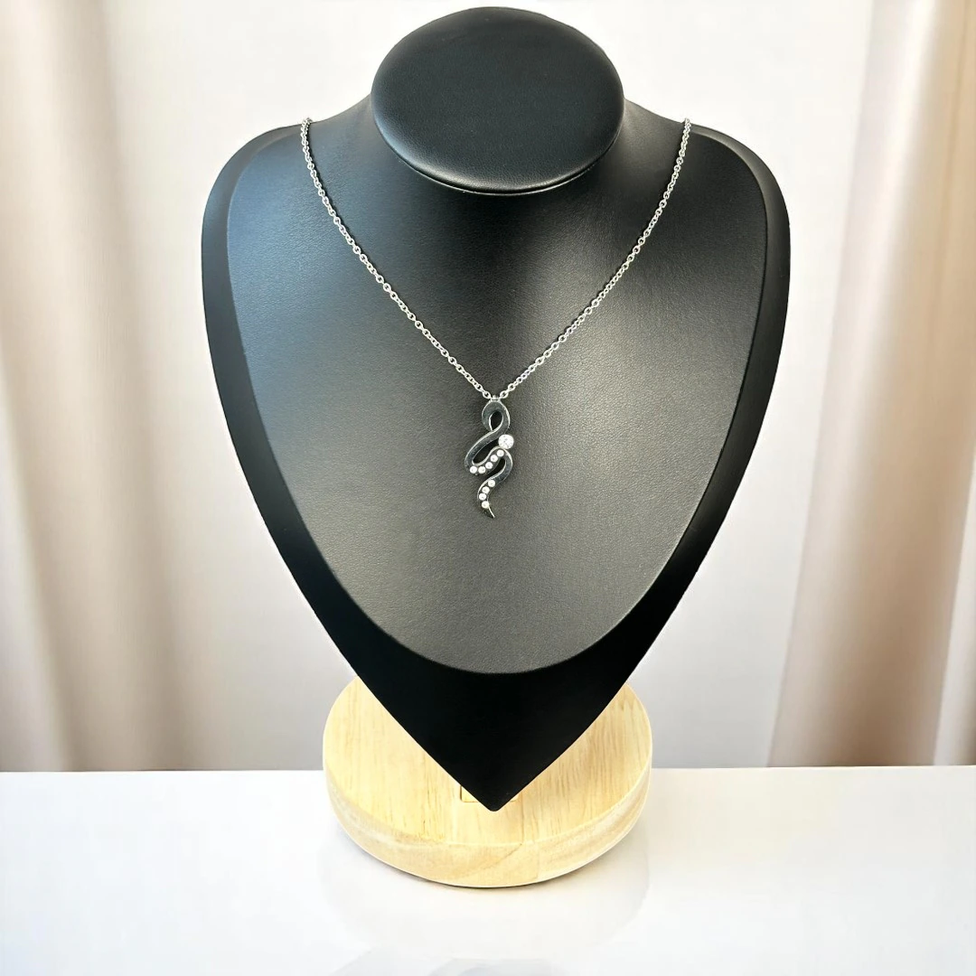 Collier pendentif sinueux foncé orné de petits cristaux sur chaîne fine argentée, buste présentoir noir