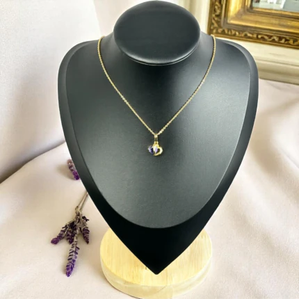 Collier pendentif cœur doré serti d'une pierre violette sur buste présentoir noir, brins de lavande