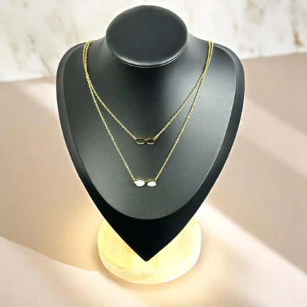 Collier multirang doré à deux chaînes fines, symbole infini uni et infini pavé de cristaux sur buste noir