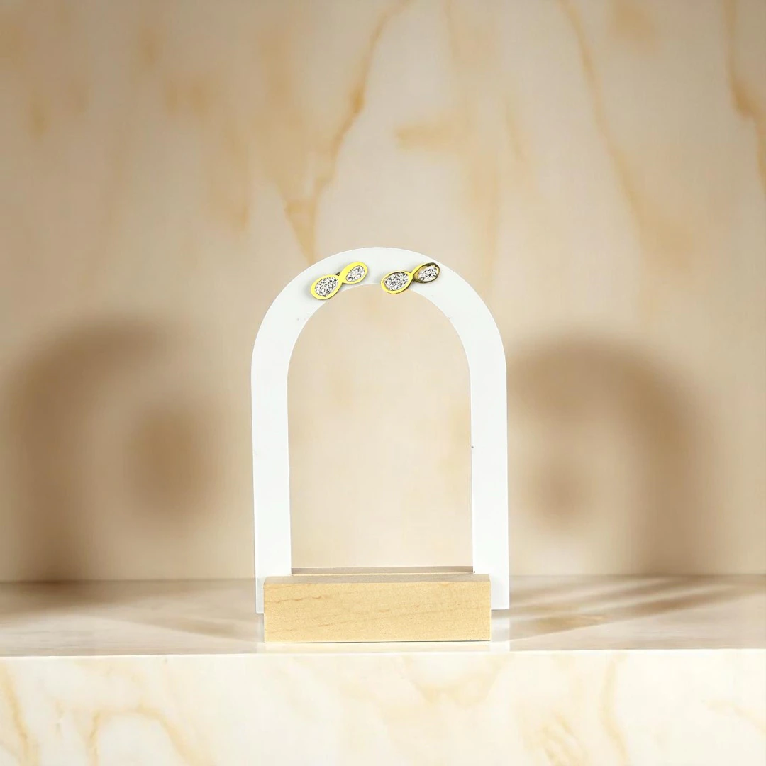 Puces d'oreilles infini dorées pavées de cristaux présentées sur un présentoir arche blanc