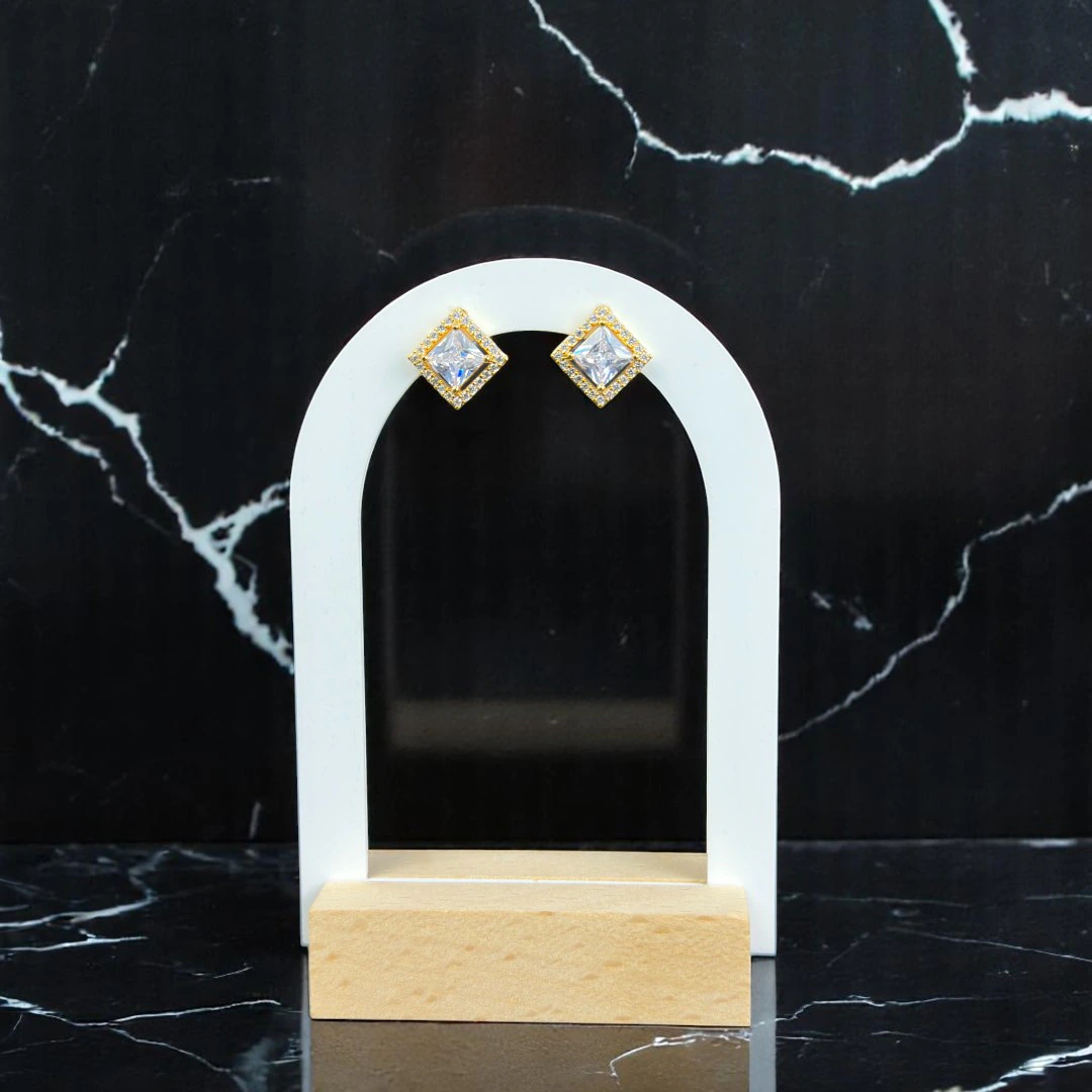 Puces d'oreilles dorées à cristal carré entouré de strass sur présentoir arche blanc