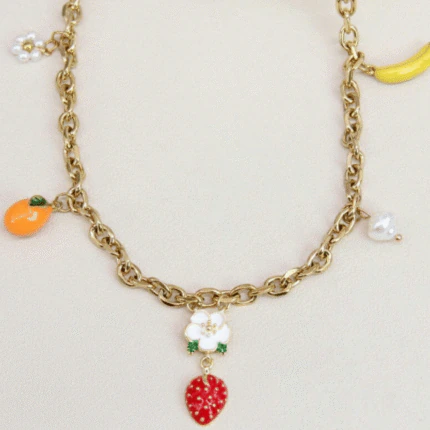 Gros plan sur la chaîne dorée à maillons et les charms fraise, orange, banane, fleurs et perle