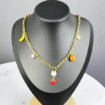 Collier chaîne dorée à breloques fruits colorés et fleurs blanches présenté sur un buste noir