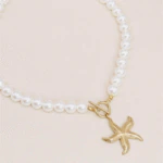 Collier perles et étoile de mer dorée vu de côté, fermoir T et rang de perles blanches sur fond beige