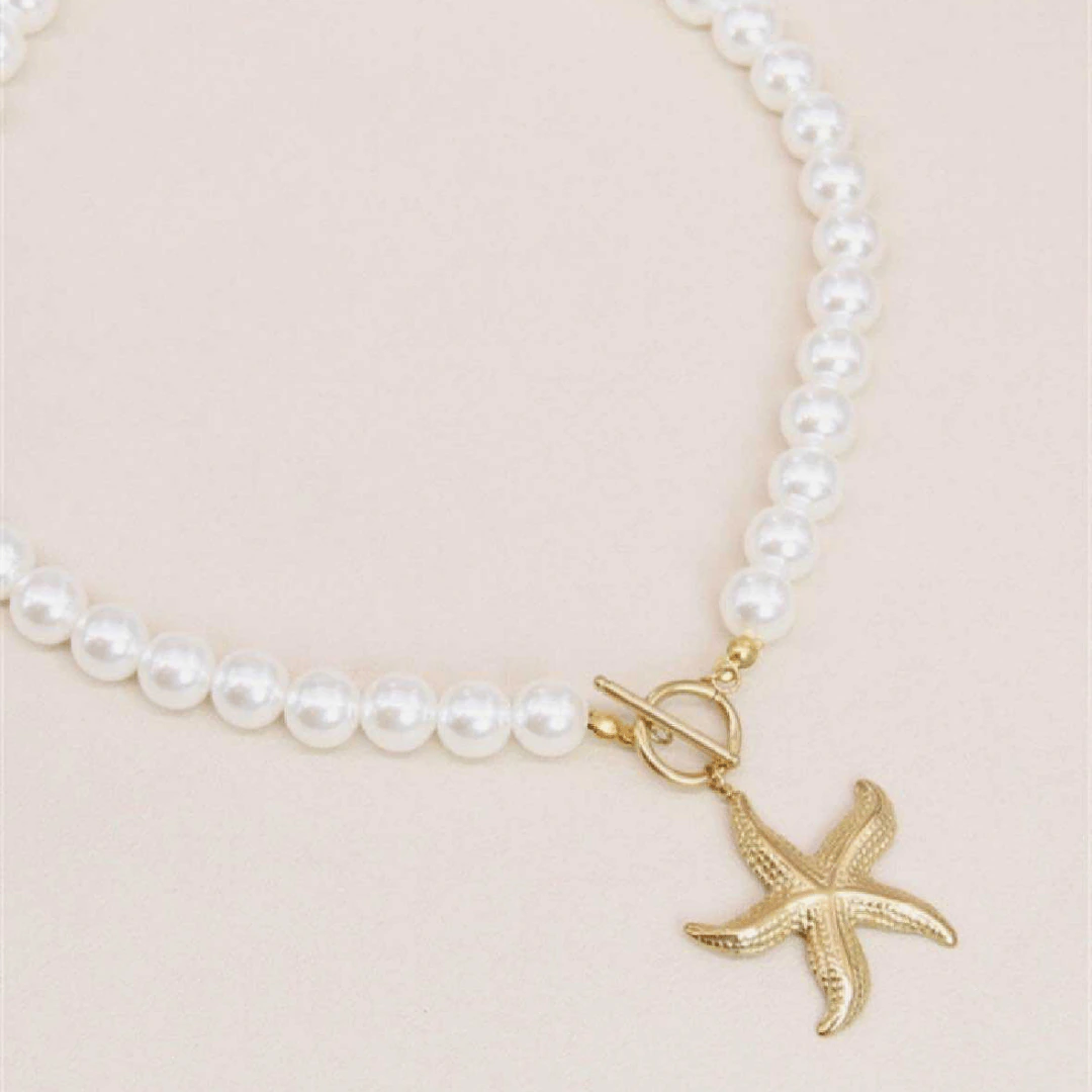 Collier perles et étoile de mer dorée vu de côté, fermoir T et rang de perles blanches sur fond beige