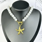 Collier de grosses perles blanches à pendentif étoile de mer doré présenté sur un buste noir
