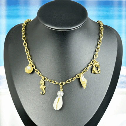 Collier chaîne dorée à breloques marines, coquillages et perles sur buste noir, fond de plage