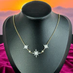 Collier trois étoiles scintillantes sur chaîne dorée présenté sur un buste noir, fond coucher de soleil