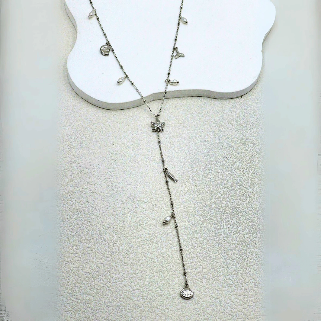 Collier long en Y argenté à étoile de mer et pendentif coquillage posé à plat sur fond blanc texturé