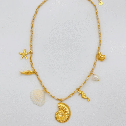Collier chaîne dorée à charms marins posé à plat : ammonite, coquillage blanc, poisson et étoile de mer
