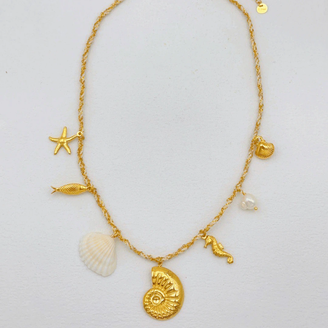 Collier chaîne dorée à charms marins posé à plat : ammonite, coquillage blanc, poisson et étoile de mer