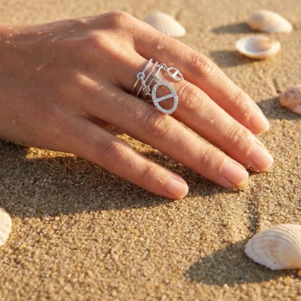 Bague femme argentée ouverte à charms ovales sertis de strass portée à la main sur le sable