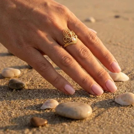 Bague femme dorée motif couronne ajourée à détail nacré portée à la main, sable et galets