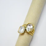 Bague femme dorée à pierres facettées transparentes rectangle et goutte, anneau multirang sur support beige