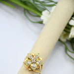 Bague femme dorée motif fleur à pierres transparentes facettées et strass sur un support beige