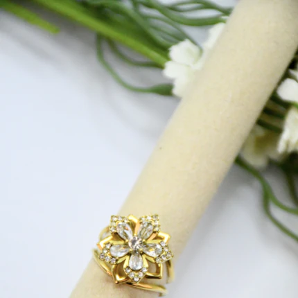 Bague femme dorée motif fleur à pierres transparentes facettées et strass sur un support beige