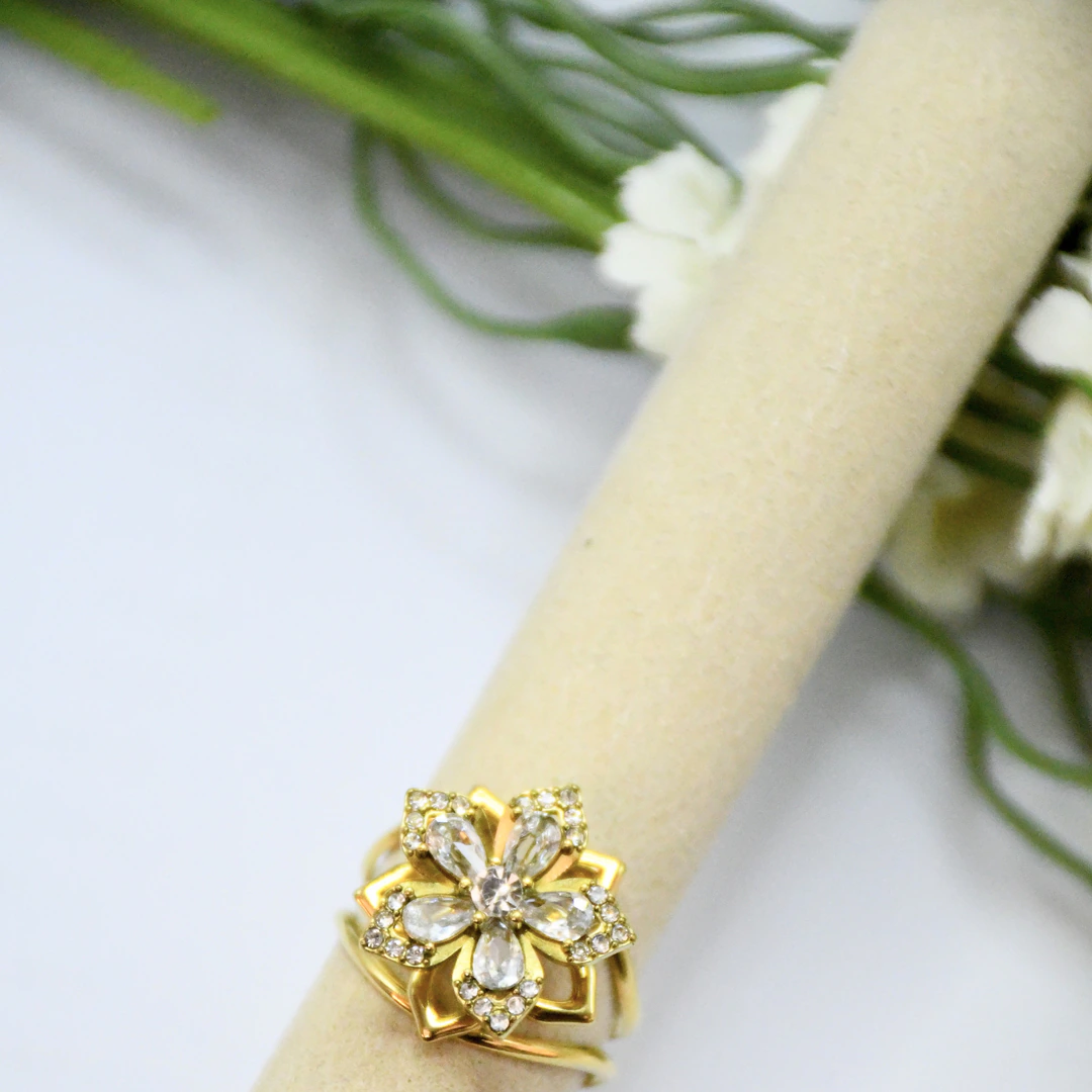LV-BG-32 Bague femme dorée motif fleur à pierres transparentes facettées et strass sur un support beige