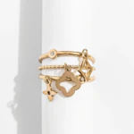 Bague dorée trois rangs avec charm trèfle ajouré, étoile et petits strass sur un support blanc
