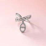 Bague femme argentée effet maillon avec charm ovale suspendu et anneaux croisés sur fond rose