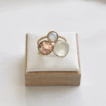 Gros plan sur la bague dorée double anneau perlé, pierre rosée facettée, pierre nacrée et pierre blanche