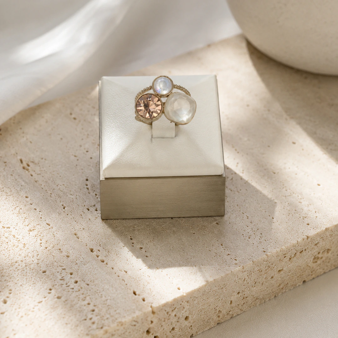 Bague dorée trois pierres effet nacré et rosé sur un présentoir cube blanc posé sur une pierre beige