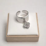 Bague ouverte argentée à anneau large et lisse avec charm trèfle suspendu sur un présentoir blanc