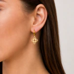 Boucles d'oreilles créoles pendantes dorées portées à l'oreille, pendentif ajouré à quatre pétales