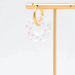 Créole dorée à pendentif fleur transparente à pois roses suspendue à un présentoir doré